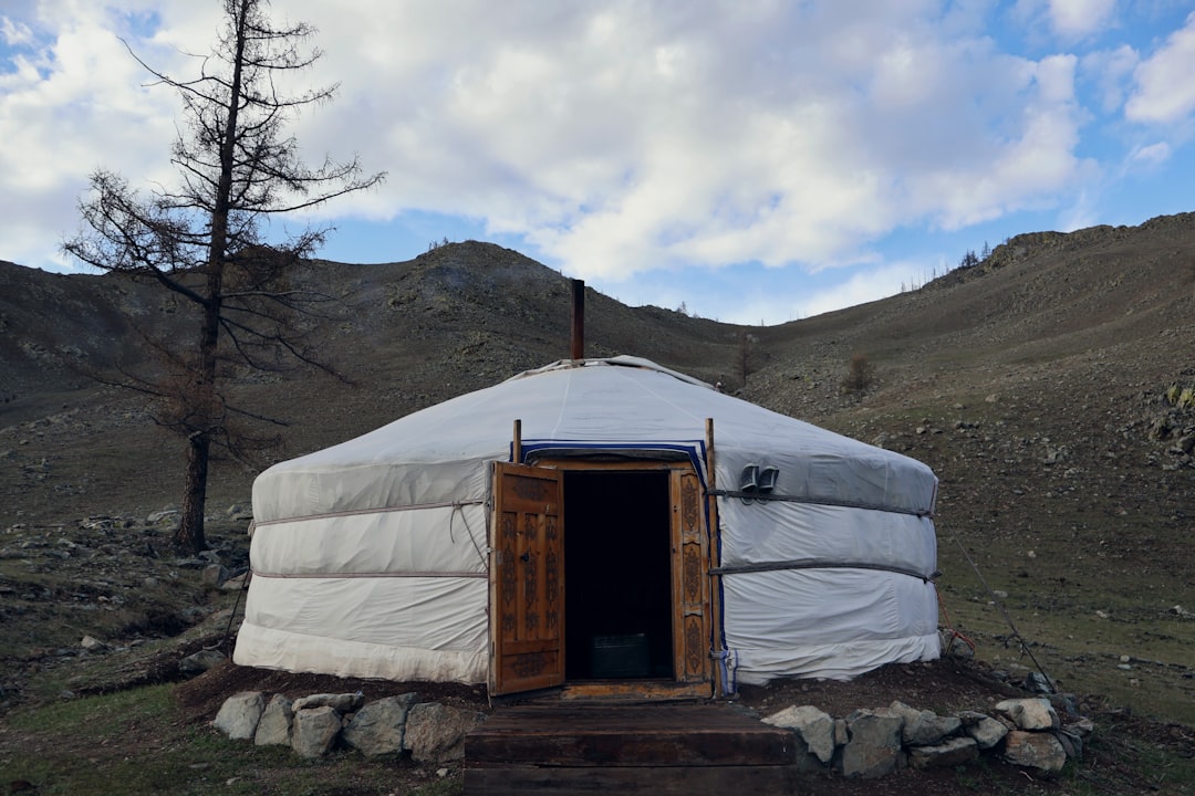 A mongolian yurt sits in a scenic, hilly landscape.